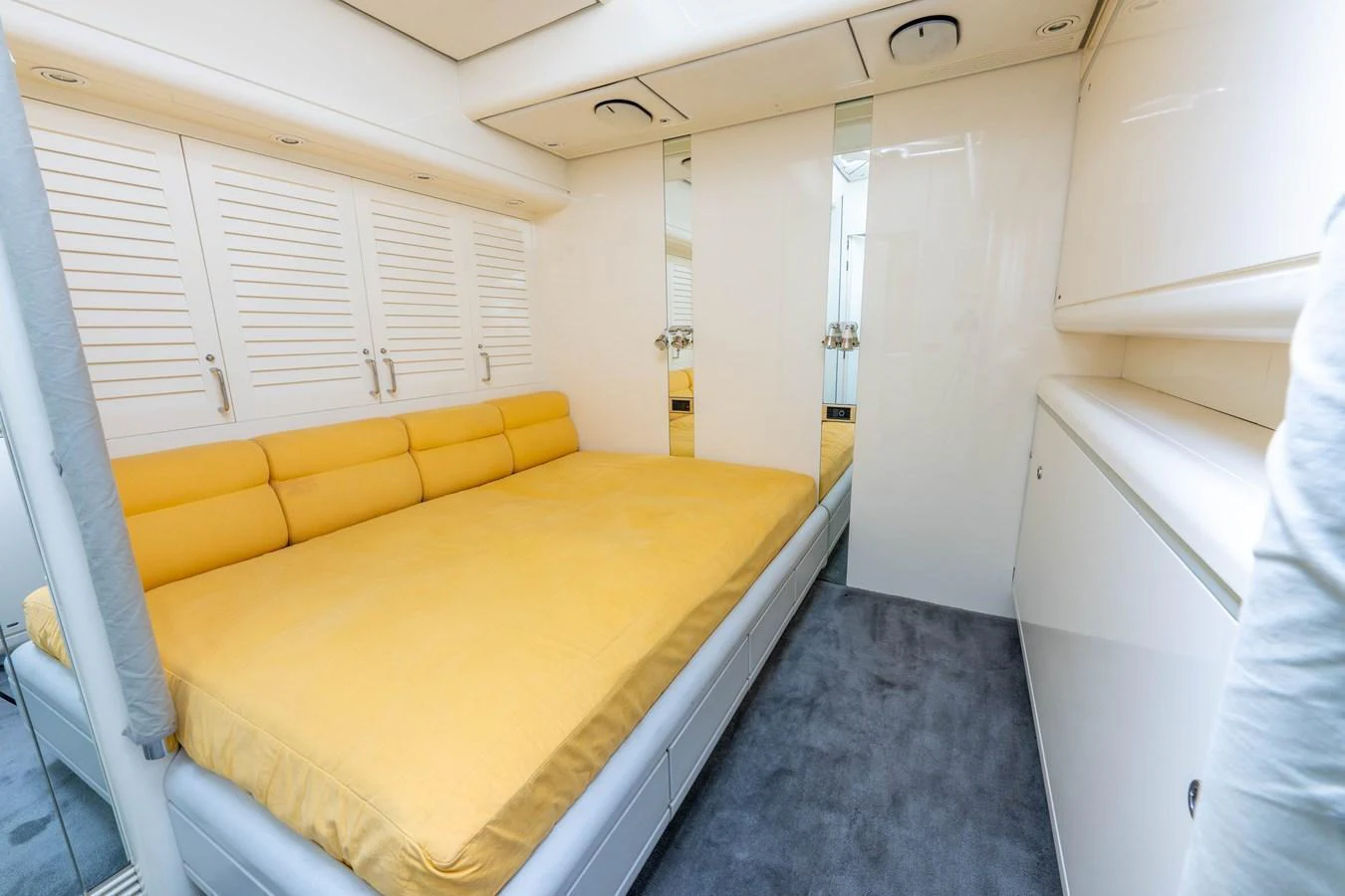The stateroom features a comfortable bed with a bright yellow cover, surrounded by sleek white cabinetry and mirrored accents. aboard CYCLOS III Yacht for Sale