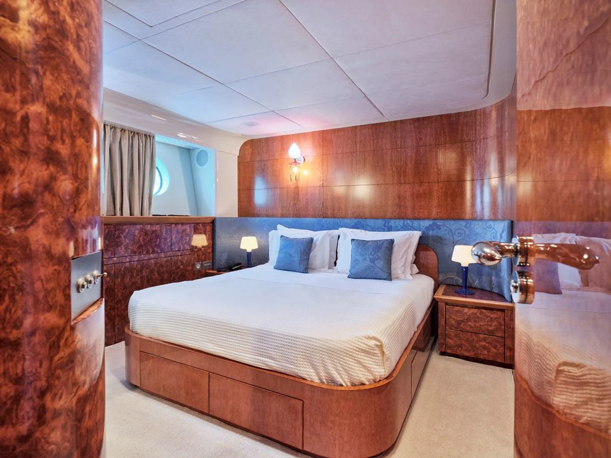 The stateroom features a luxurious bed with elegant wood paneling and soft lighting. aboard CONDOR A Yacht for Sale