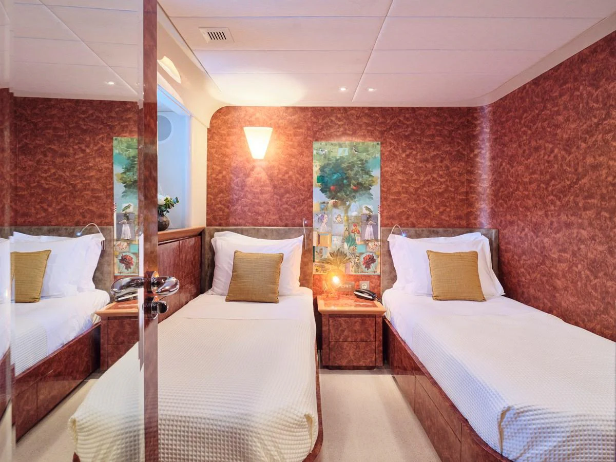 A cozy twin stateroom featuring two single beds with elegant decor and warm lighting. aboard CONDOR A Yacht for Sale