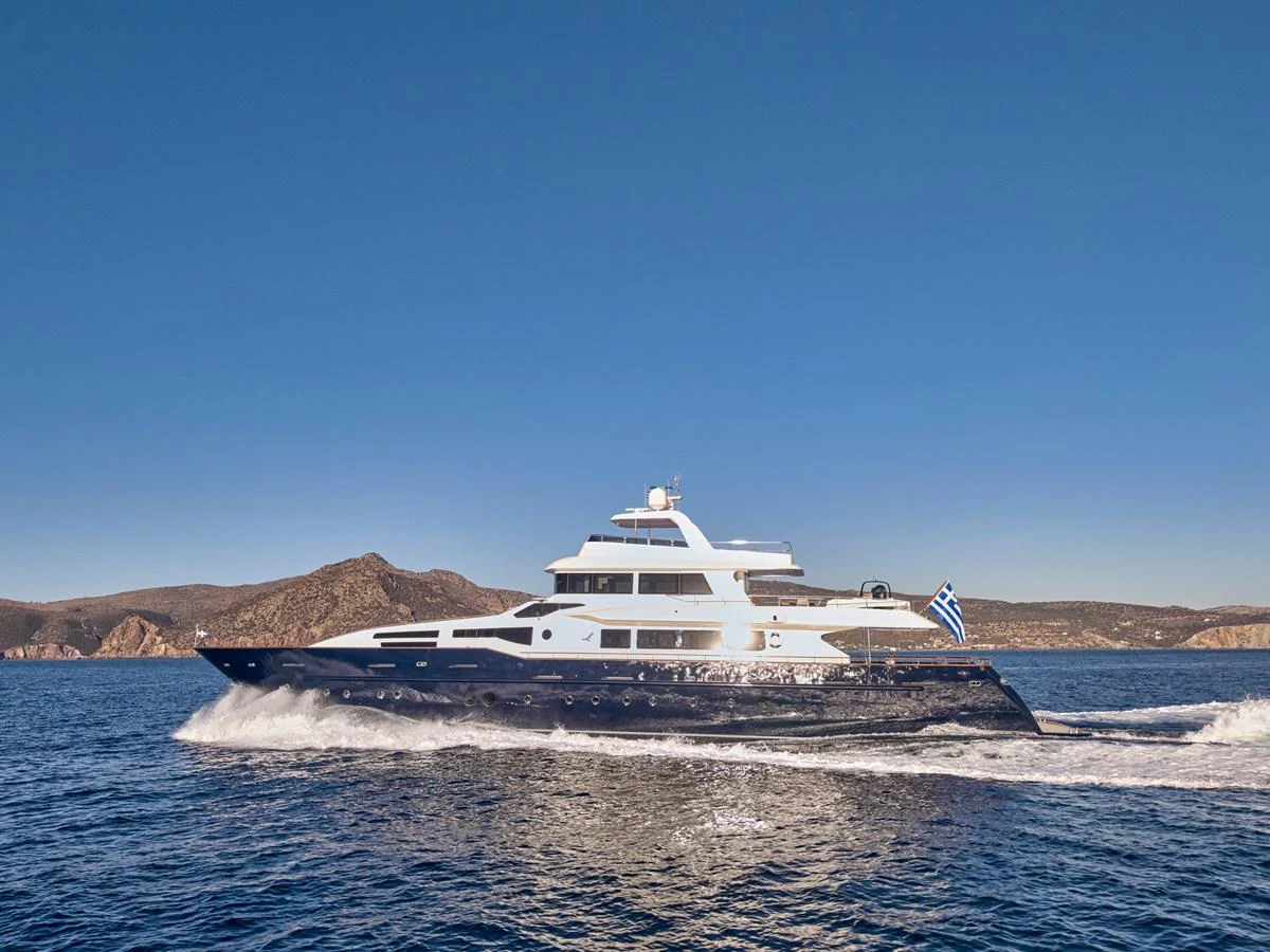 A sleek yacht cruises through the water against a backdrop of scenic coastal mountains. aboard CONDOR A Yacht for Sale