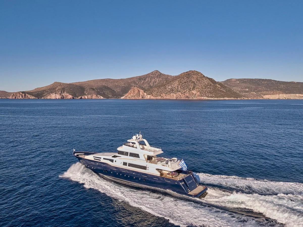 A sleek yacht cruises through open waters with a scenic mountainous backdrop. aboard CONDOR A Yacht for Sale