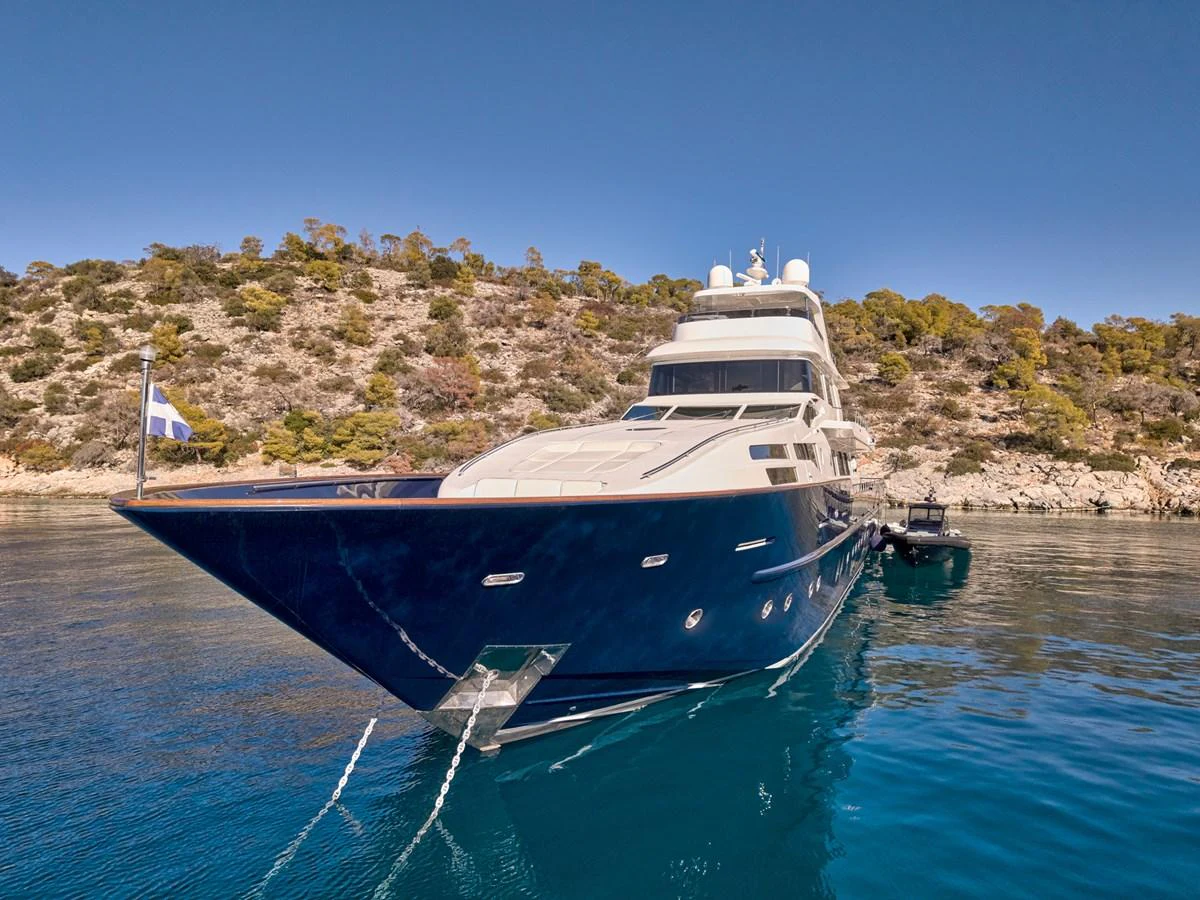 A sleek and elegant yacht is anchored in a serene bay with clear blue waters and a scenic backdrop. aboard CONDOR A Yacht for Sale