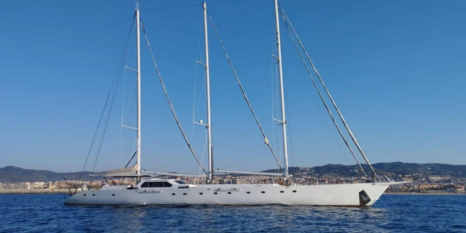 A sleek, modern sailing yacht glides gracefully on the water against a backdrop of a coastal city. aboard YAMAKAY Yacht for Sale
