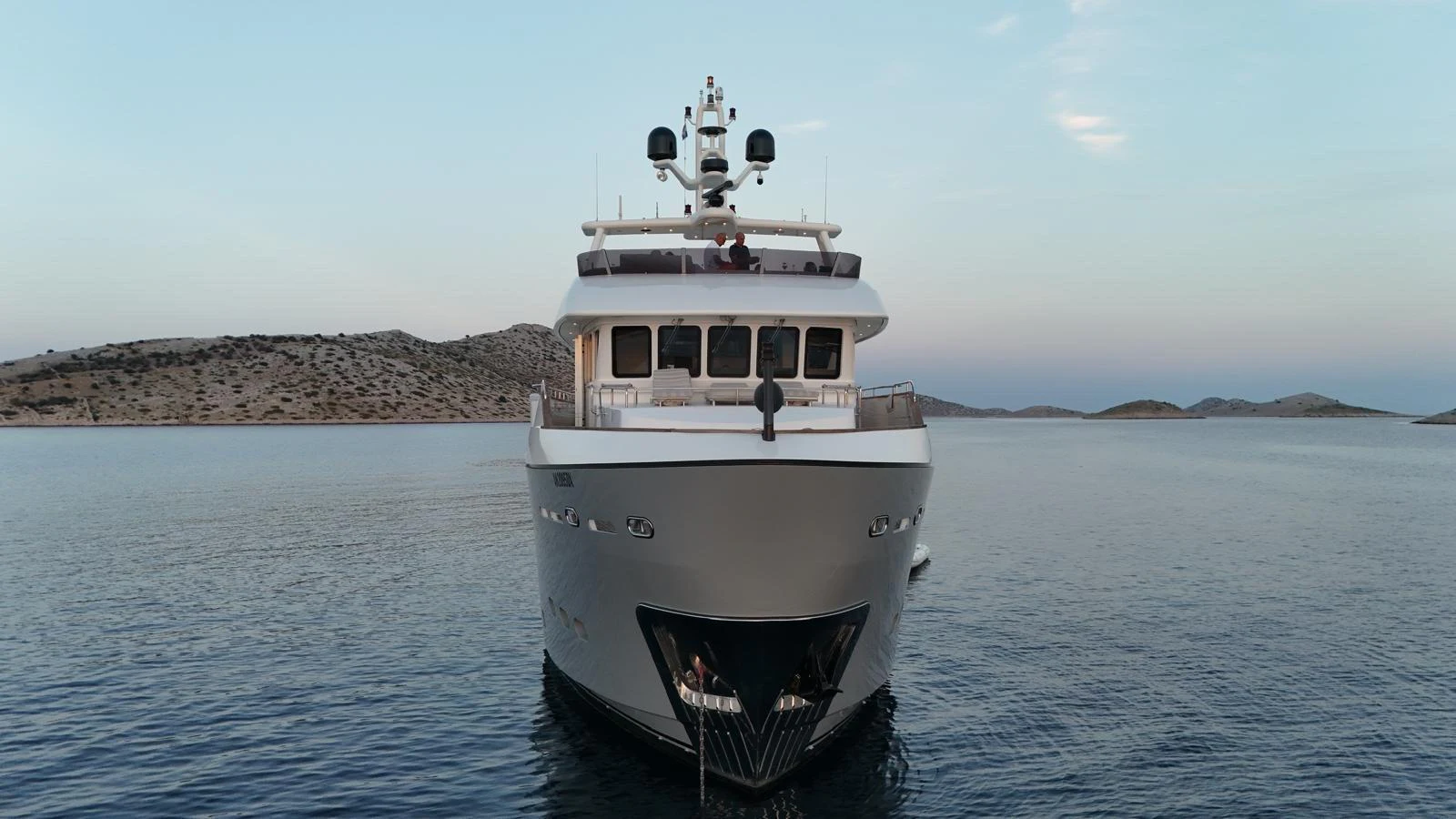 A luxurious yacht is anchored in calm waters with a scenic backdrop of distant hills. aboard GRANIL Yacht for Sale