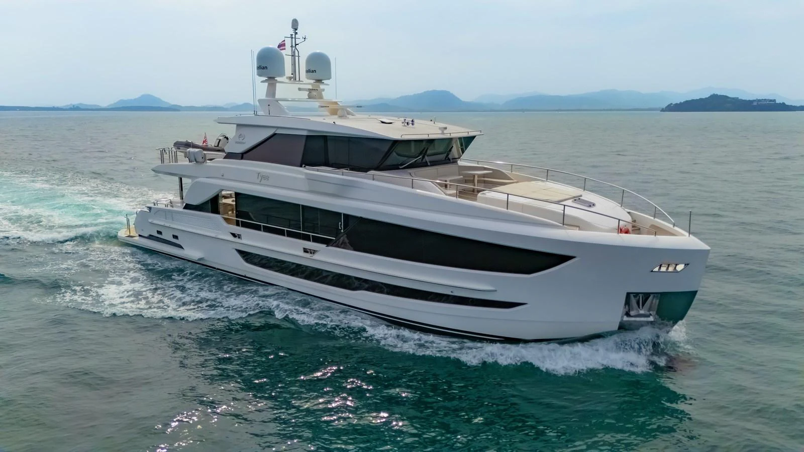 A sleek, modern yacht cruises through calm waters with a scenic backdrop of distant islands. aboard AVELINE Yacht for Sale
