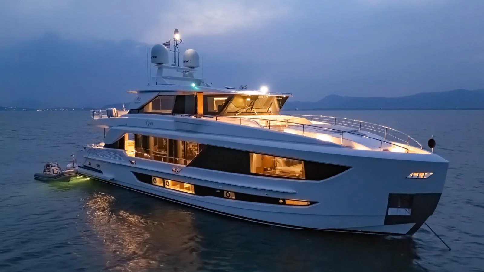 This sleek yacht is beautifully illuminated, showcasing its modern design and luxurious features as it rests on the water at dusk. aboard AVELINE Yacht for Sale