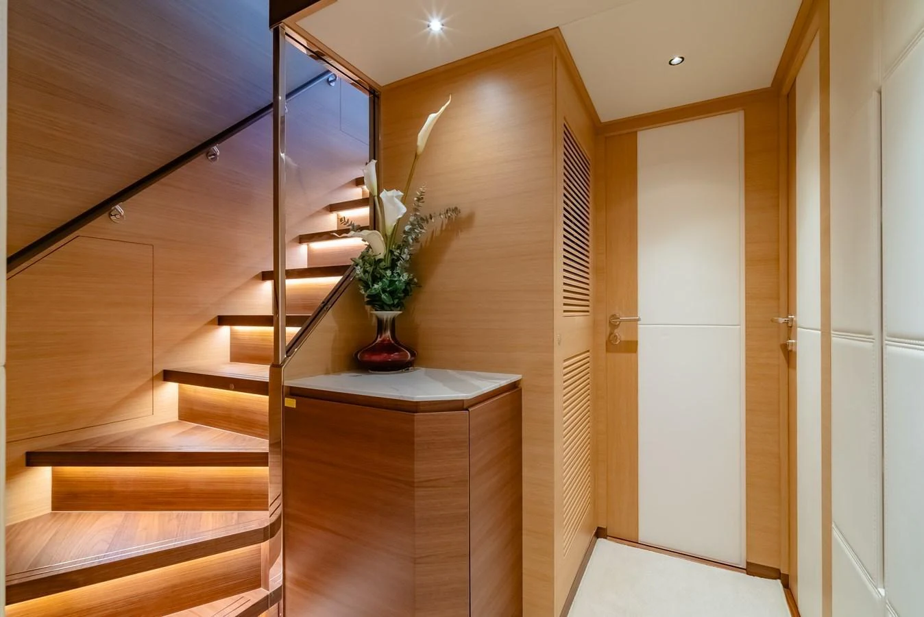 A beautifully lit staircase area with elegant wood paneling and a decorative vase. aboard AVELINE Yacht for Sale