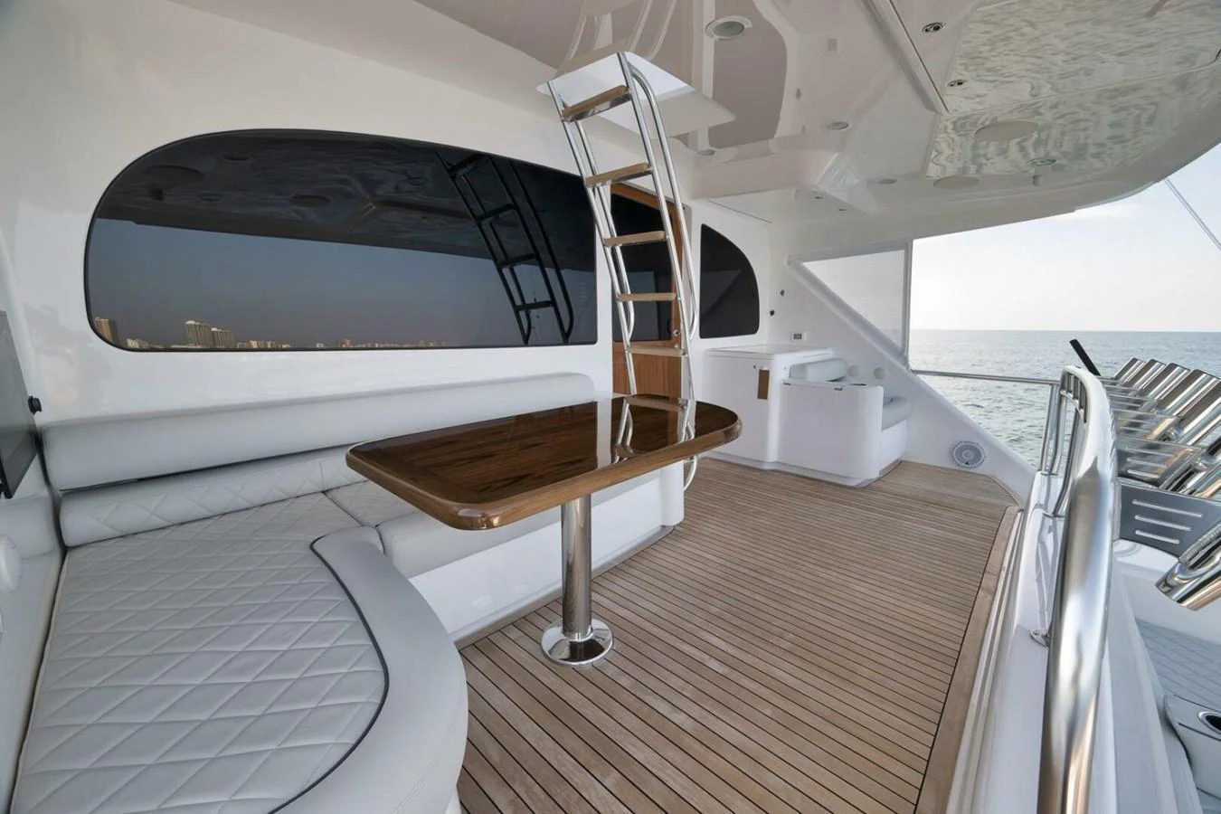 The aft deck features a sleek seating area with a polished wooden table and a modern ladder leading to the upper deck. aboard NIKKI BELLA Yacht for Sale