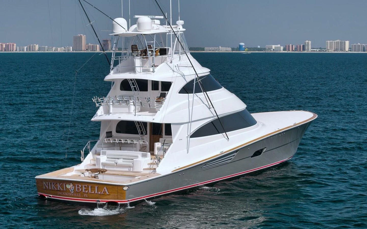 A sleek yacht cruises through calm waters with a cityscape in the background. aboard NIKKI BELLA Yacht for Sale