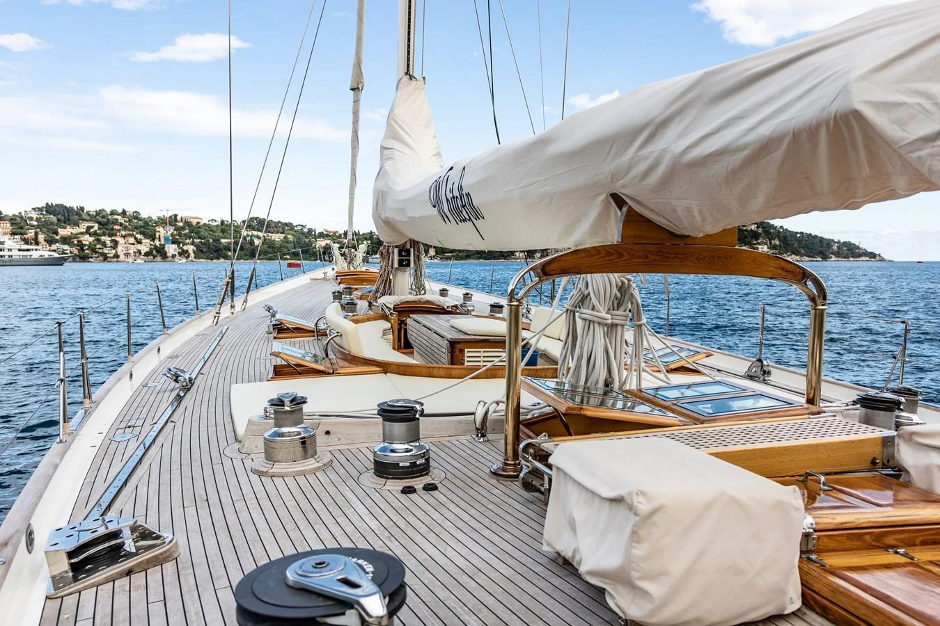 The yacht's deck features elegant woodwork and well-maintained sailing equipment, set against a serene coastal backdrop. aboard WHITEFIN Yacht for Sale