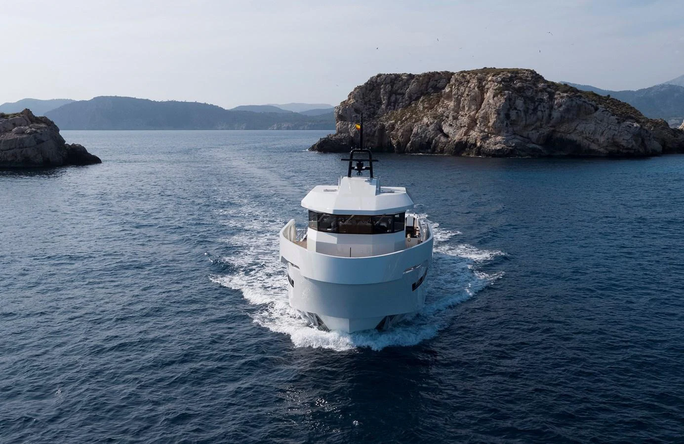A modern yacht cruises through serene waters, framed by rocky islands in the background. aboard 27 YXT Yacht for Sale