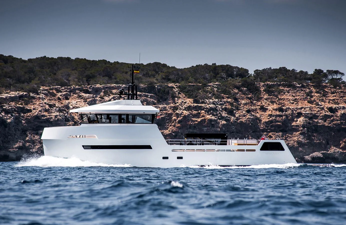 A sleek, modern yacht cruises along the coastline with a rugged landscape in the background. aboard 27 YXT Yacht for Sale