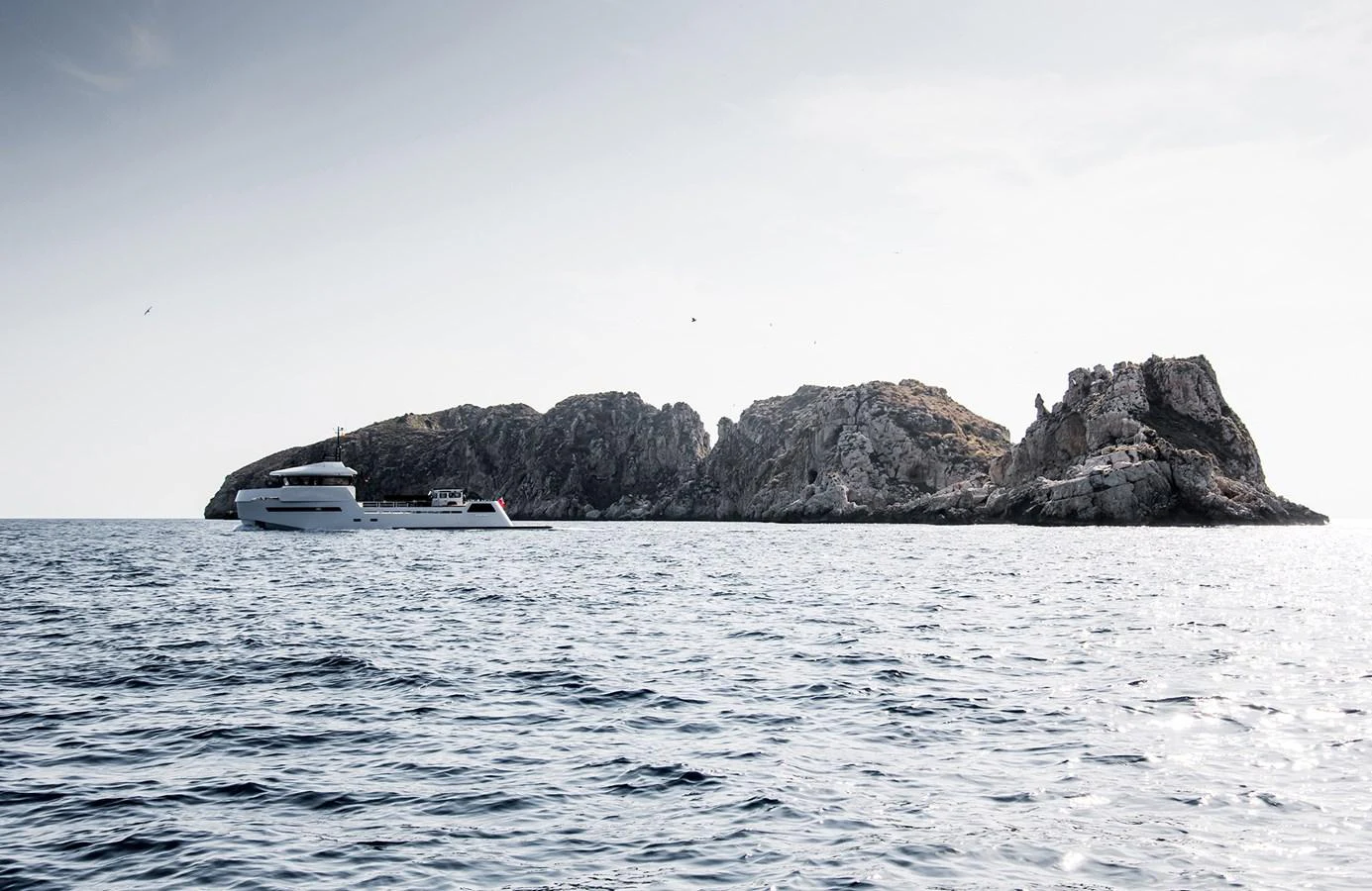 A sleek yacht cruises near a rocky island under a clear sky. aboard 27 YXT Yacht for Sale