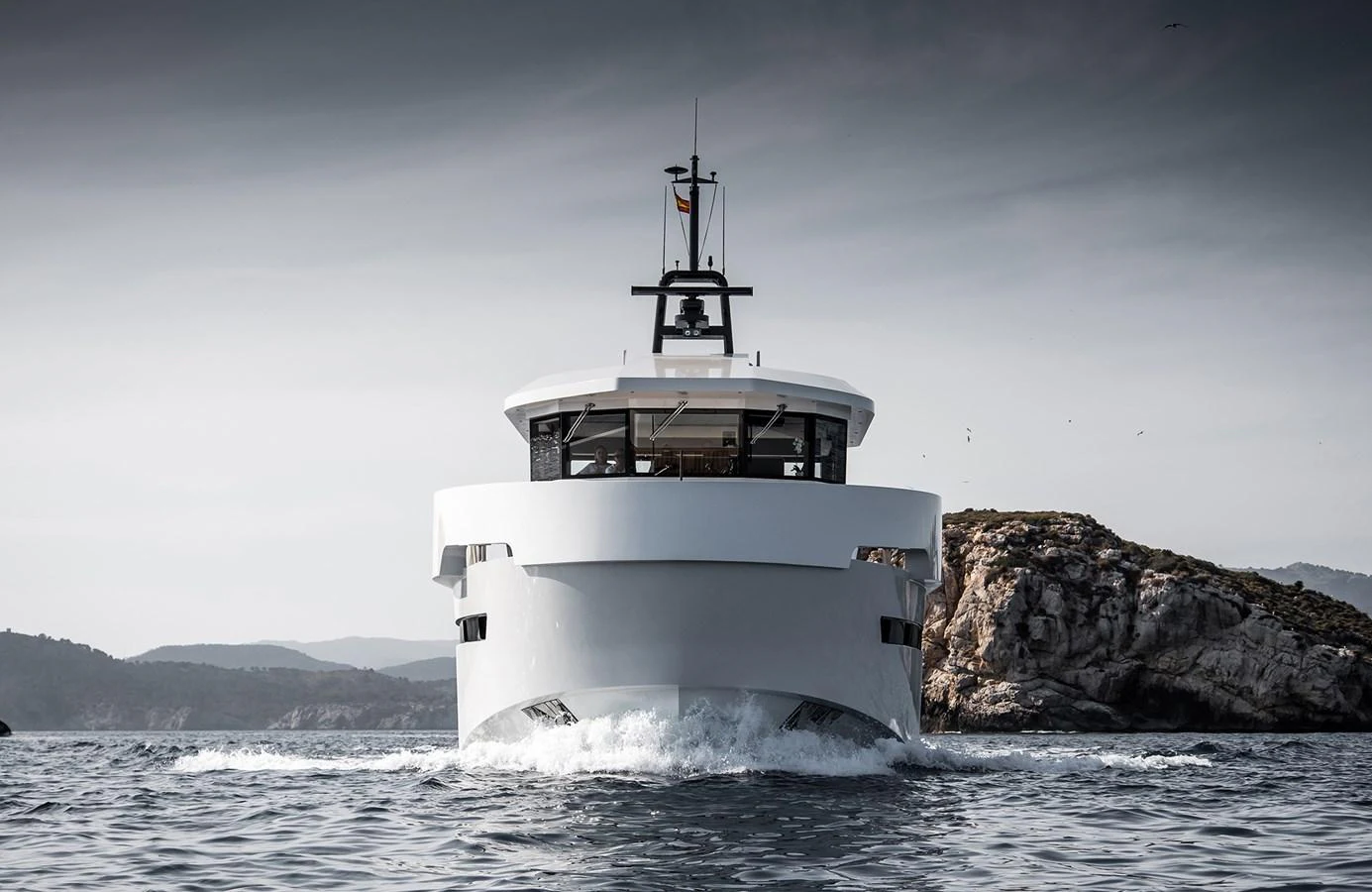 A modern yacht cruises forward with a striking and sleek design against a scenic coastal backdrop. aboard 27 YXT Yacht for Sale