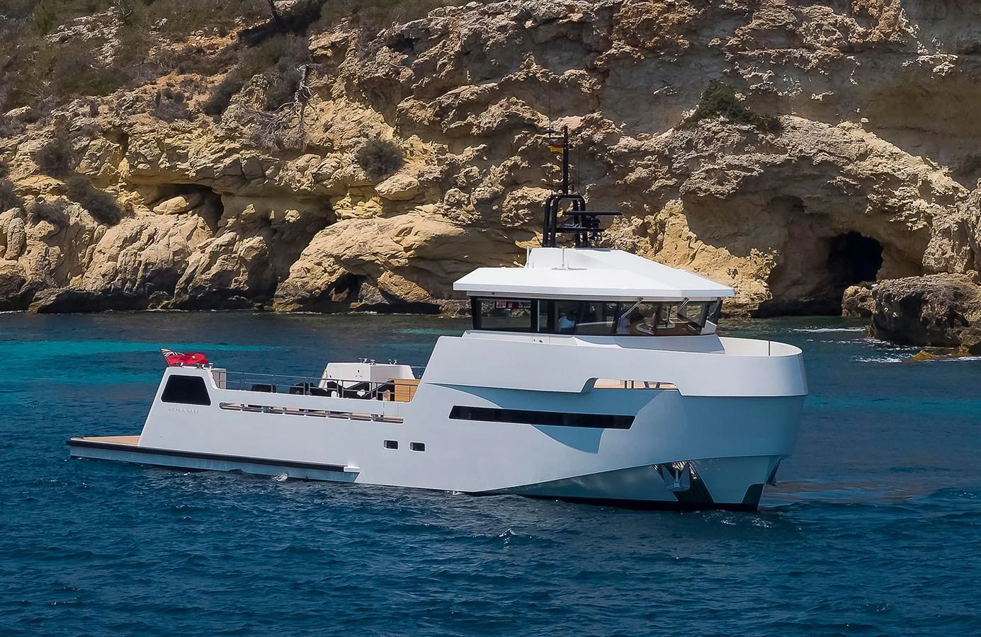 A sleek, modern yacht cruises along a rocky coastline with clear blue waters. aboard 27 YXT Yacht for Sale