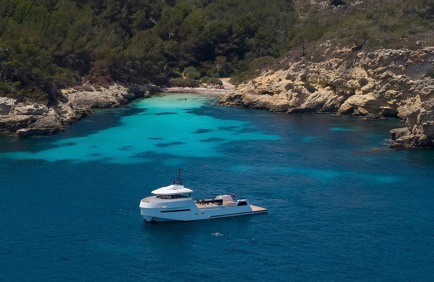 A sleek yacht is anchored in a serene, turquoise cove surrounded by rocky cliffs and lush greenery. aboard 27 YXT Yacht for Sale