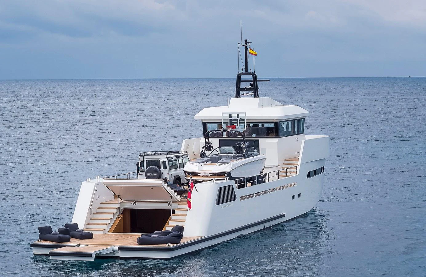 A sleek, modern yacht with an open aft deck featuring a tender and a vehicle, set against a serene ocean backdrop. aboard 27 YXT Yacht for Sale