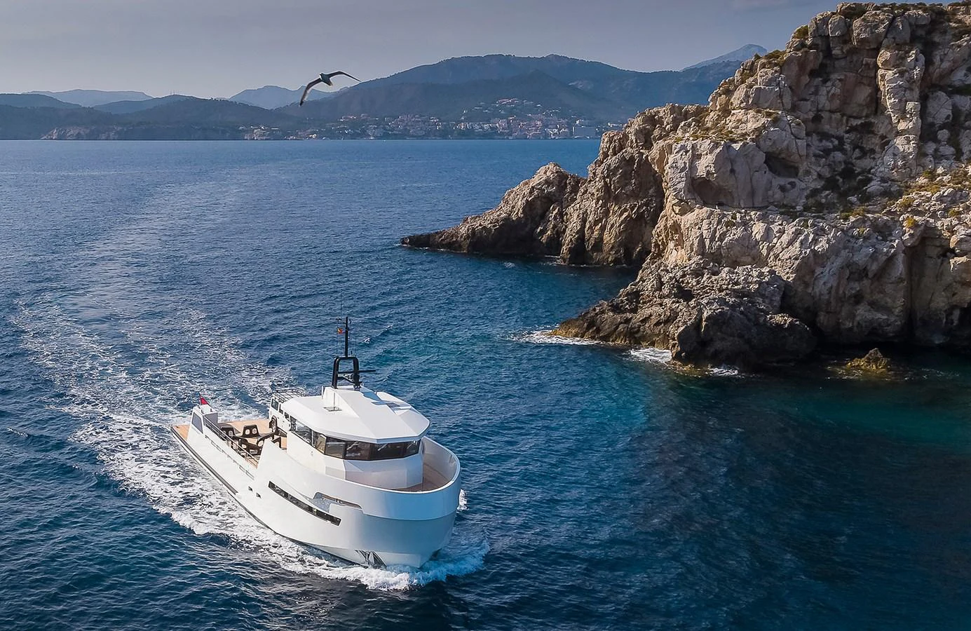 A sleek yacht cruises along a rocky coastline under a clear sky. aboard 27 YXT Yacht for Sale