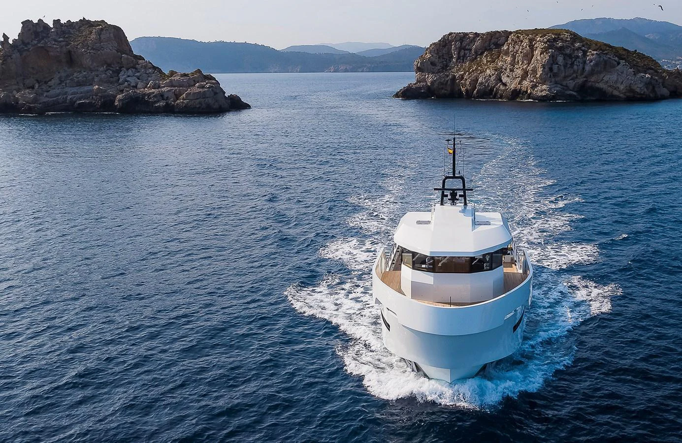 A sleek yacht cruises through calm waters between rocky islands. aboard 27 YXT Yacht for Sale