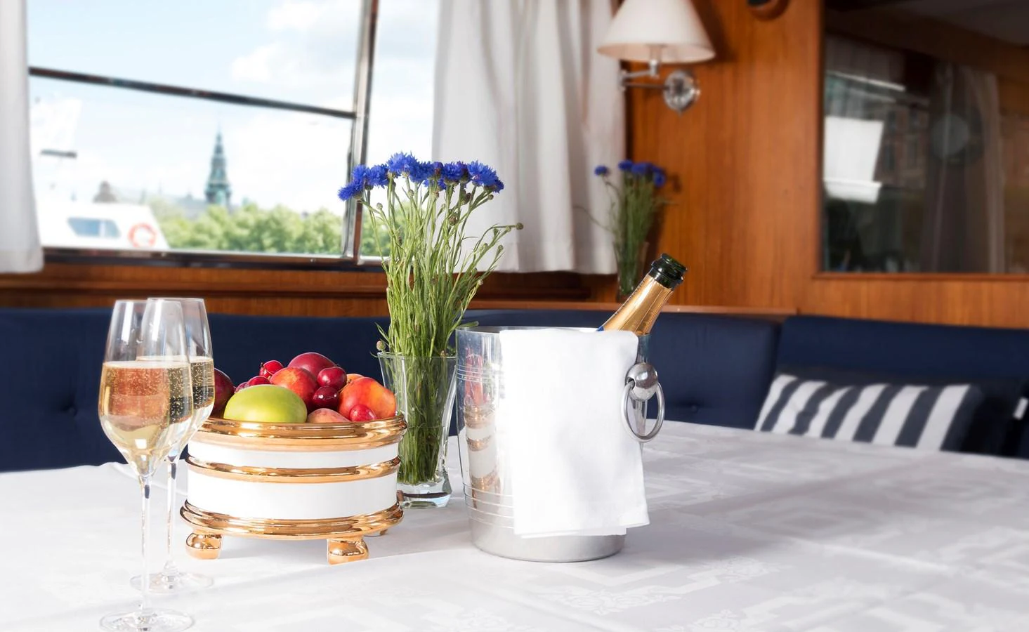 A cozy interior dining area with a table set for a delightful meal, featuring fresh flowers, fruit, and champagne. aboard STELLA NOVA Yacht for Sale