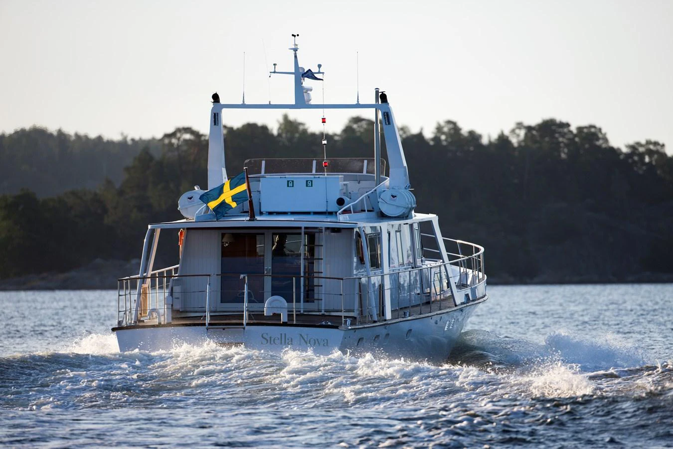A yacht cruises through calm waters with a scenic backdrop of trees. aboard STELLA NOVA Yacht for Sale