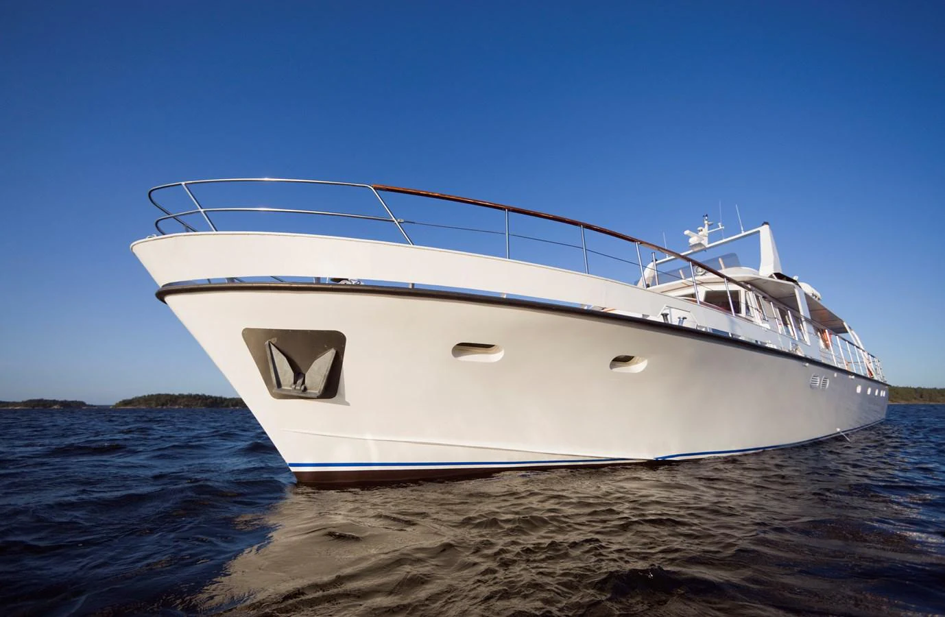 A sleek white yacht glides gracefully on calm waters under a clear blue sky. aboard STELLA NOVA Yacht for Sale