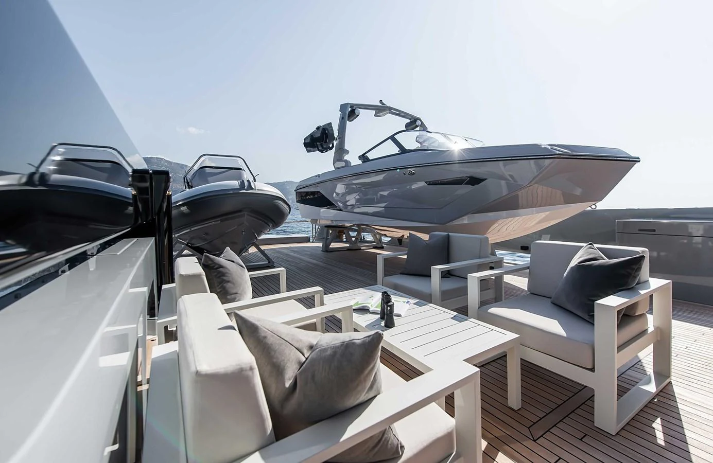 The aft deck features a comfortable seating area with modern furniture and a tender boat in the background. aboard 27 CROSSOVER Yacht for Sale