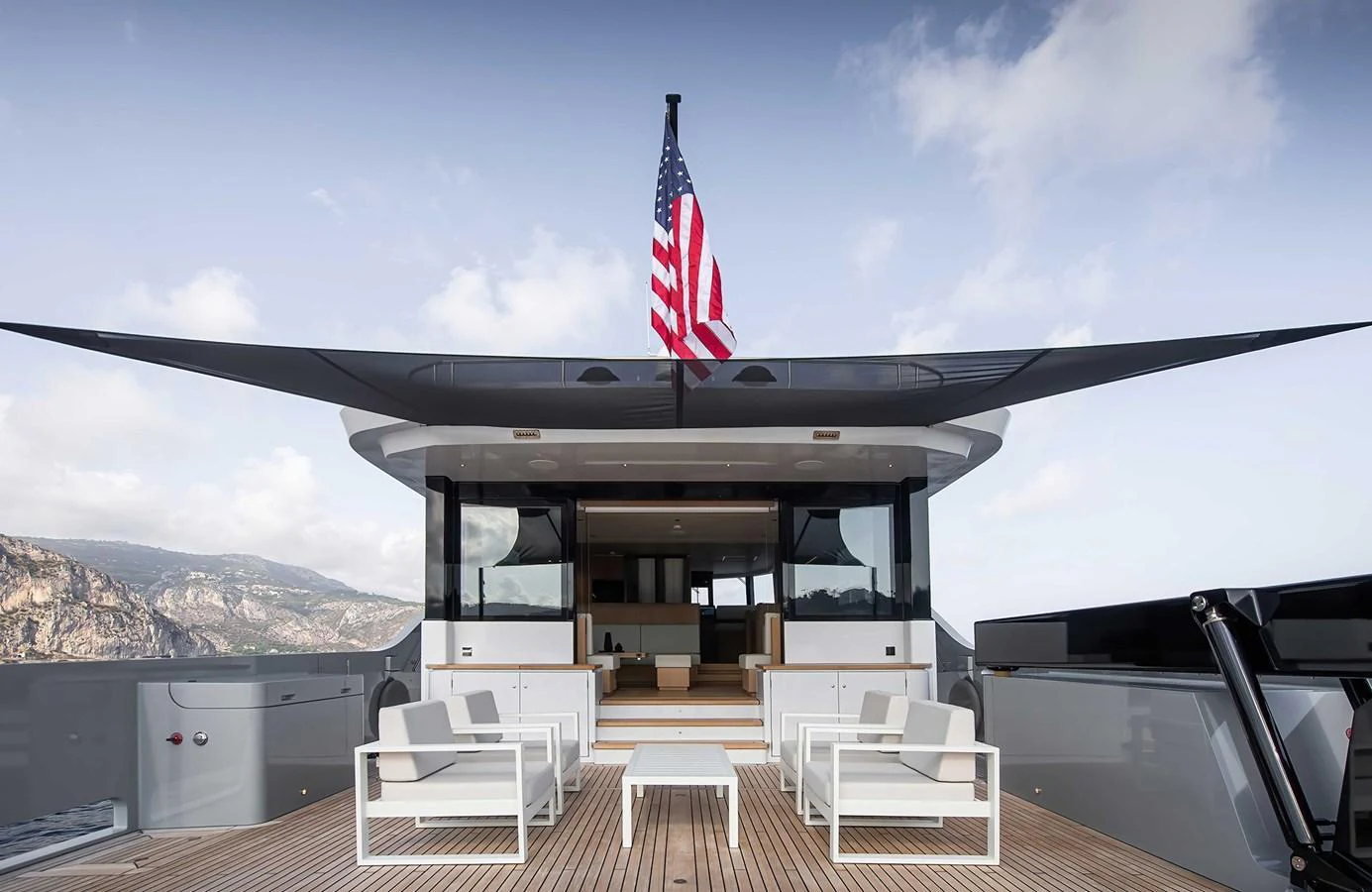 The aft deck of this yacht features modern seating and a prominent flag, set against a scenic backdrop. aboard 27 CROSSOVER Yacht for Sale