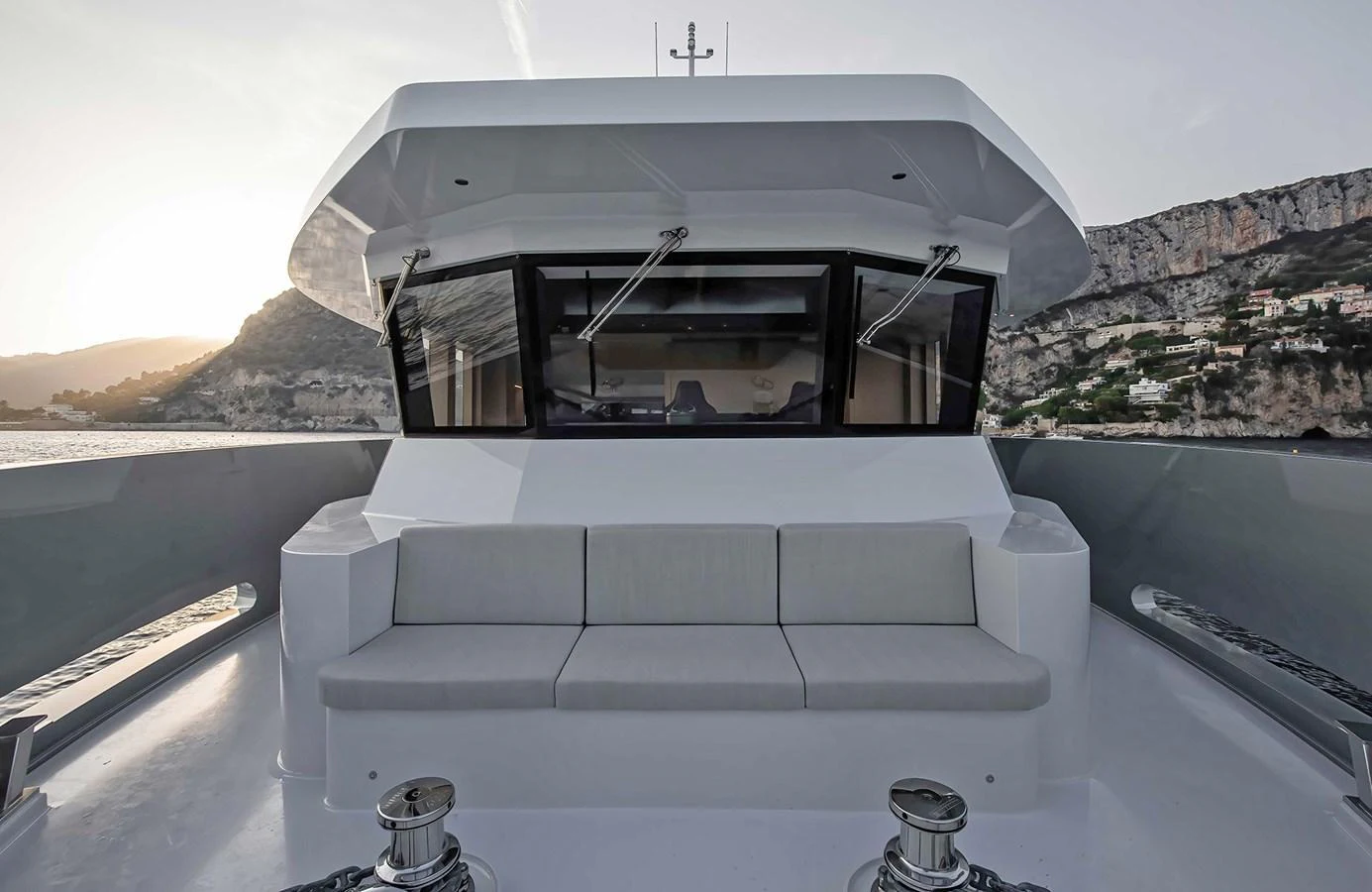 The yacht's exterior features a spacious seating area with a stunning backdrop of coastal cliffs. aboard 27 CROSSOVER Yacht for Sale