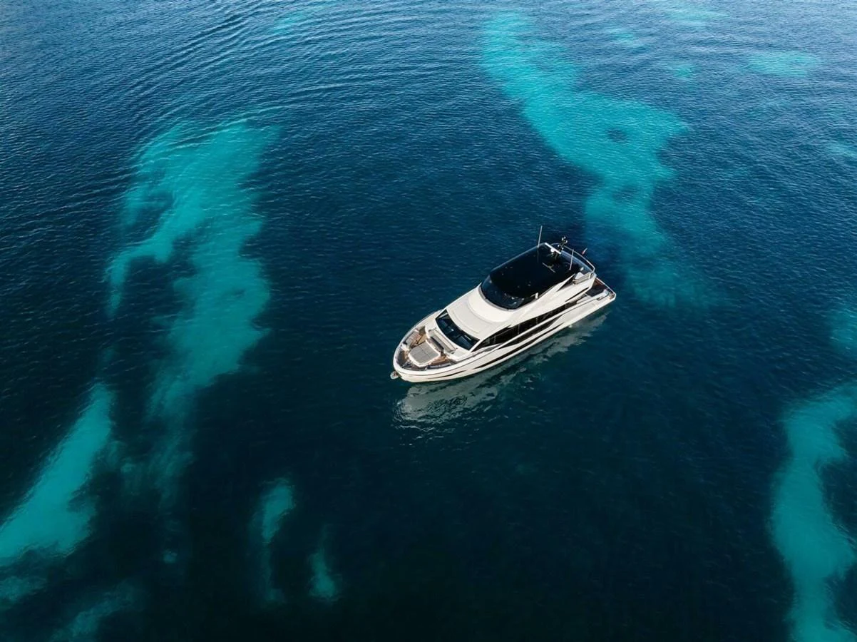 A sleek yacht cruises through clear, turquoise waters, showcasing its elegant design from an aerial perspective. aboard 90 OCEAN ENCLOSED Yacht for Sale
