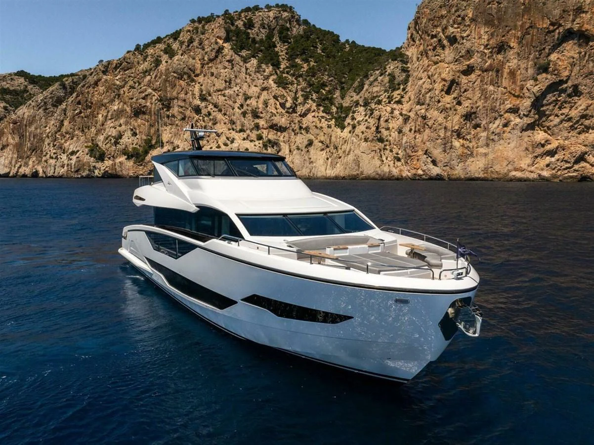 A sleek, modern yacht cruises through clear blue waters with a rocky coastline in the background. aboard 90 OCEAN ENCLOSED Yacht for Sale