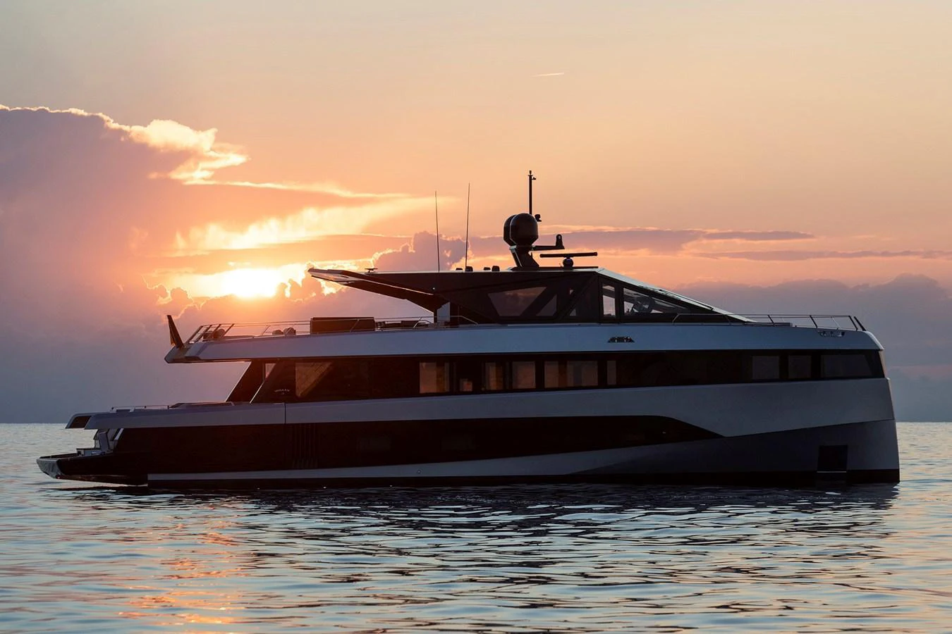 A sleek yacht is silhouetted against a stunning sunset on calm waters. aboard WALLYWHY200 Yacht for Sale