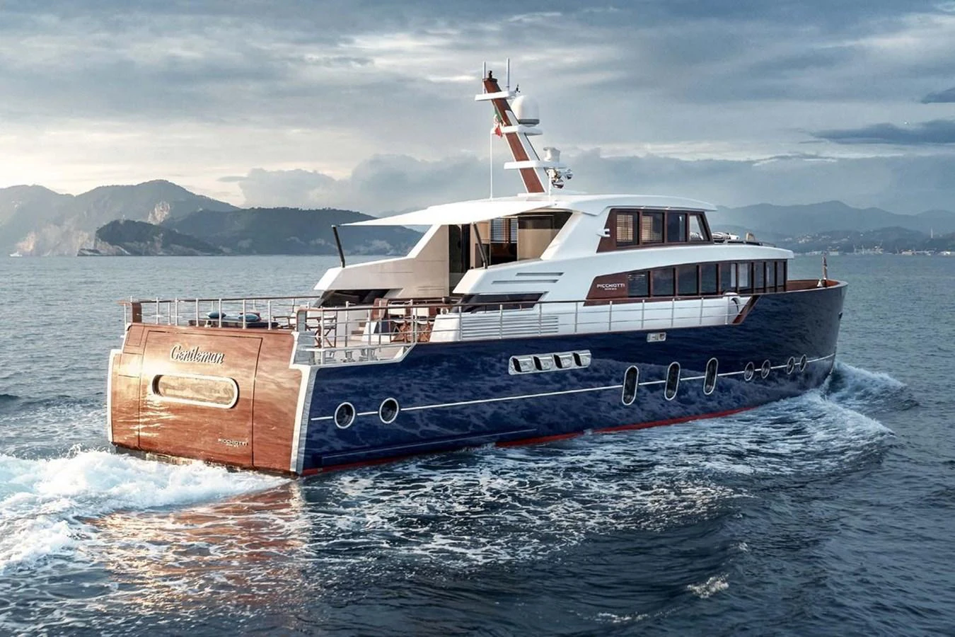 A luxurious yacht cruises through serene waters with a scenic mountainous backdrop. aboard PICCHIOTTI 24 Yacht for Sale
