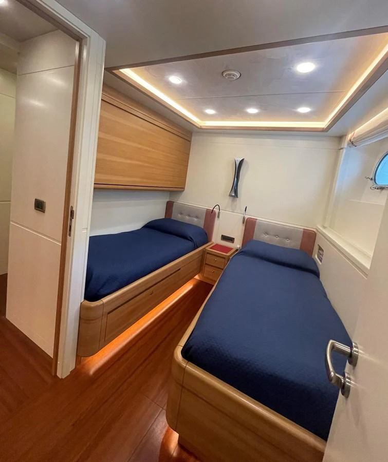 The twin stateroom features two single beds with blue bedding, warm wood accents, and modern lighting. aboard STELLA DEL NORD Yacht for Sale