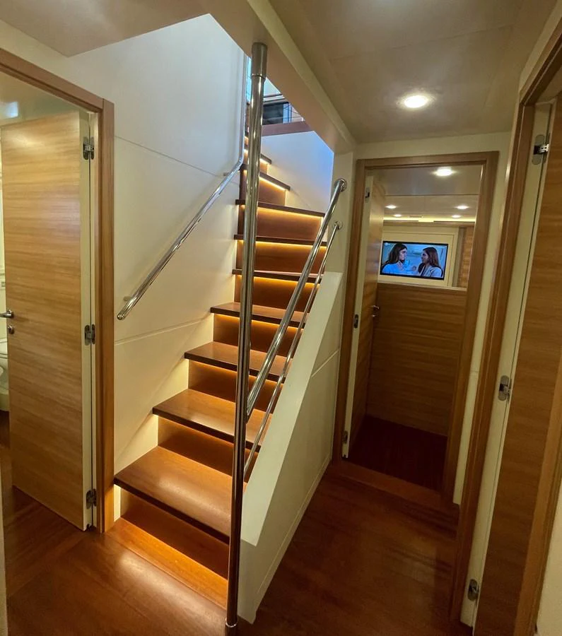 A well-lit stairway with wooden steps and stainless steel handrails leads to the upper deck. aboard STELLA DEL NORD Yacht for Sale
