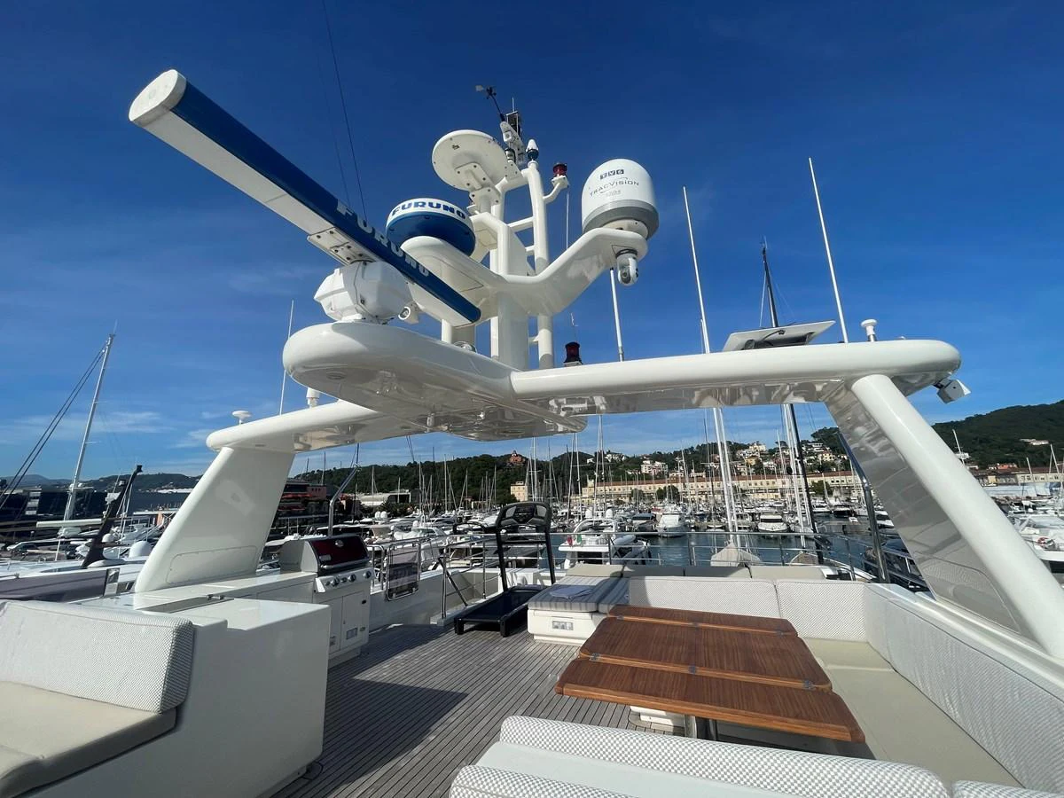 The flybridge offers a spacious area with a dining table and advanced navigation equipment under a clear blue sky. aboard STELLA DEL NORD Yacht for Sale