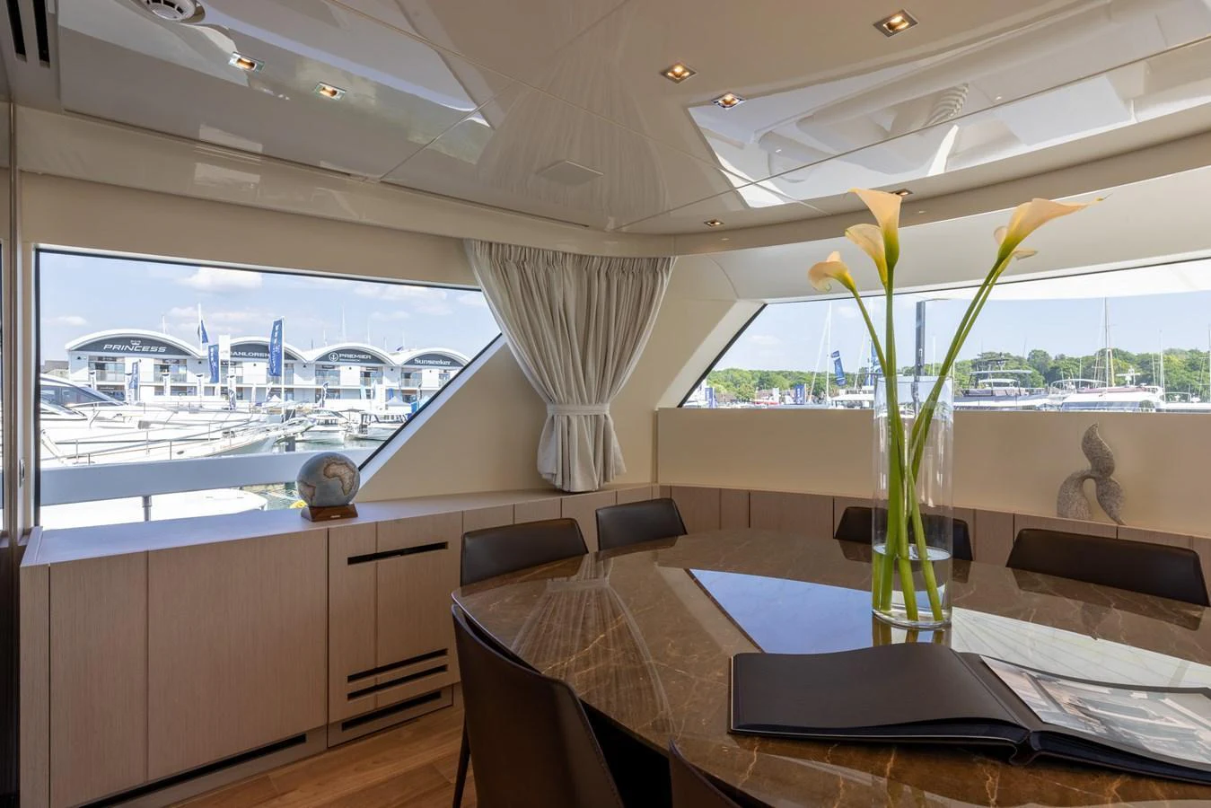 The yacht's dining area features a large table with a view of the marina through expansive windows. aboard SX76 #144 Yacht for Sale