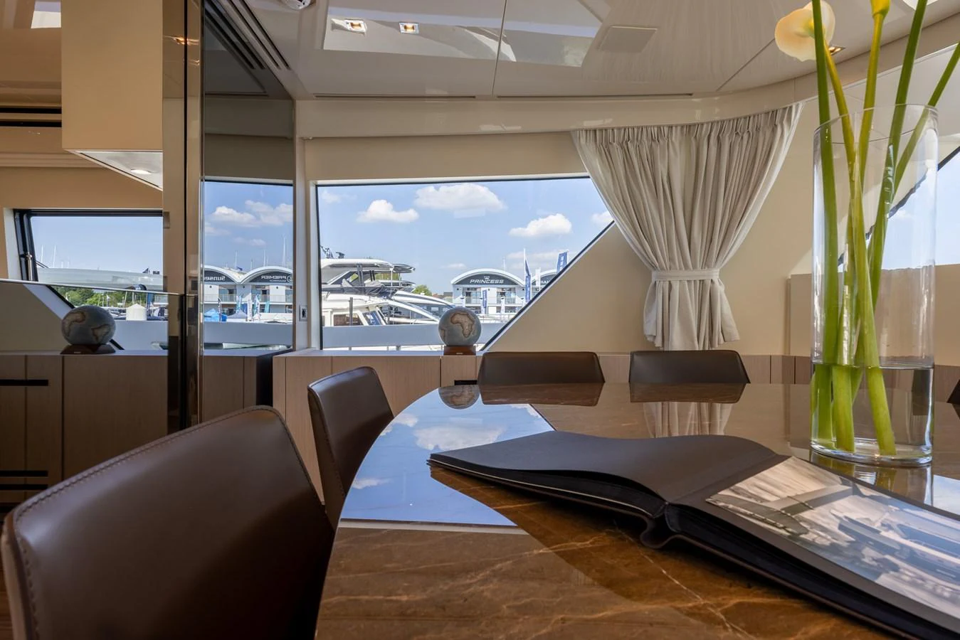 The yacht's dining area features a polished table with a view of the marina through large windows. aboard SX76 #144 Yacht for Sale