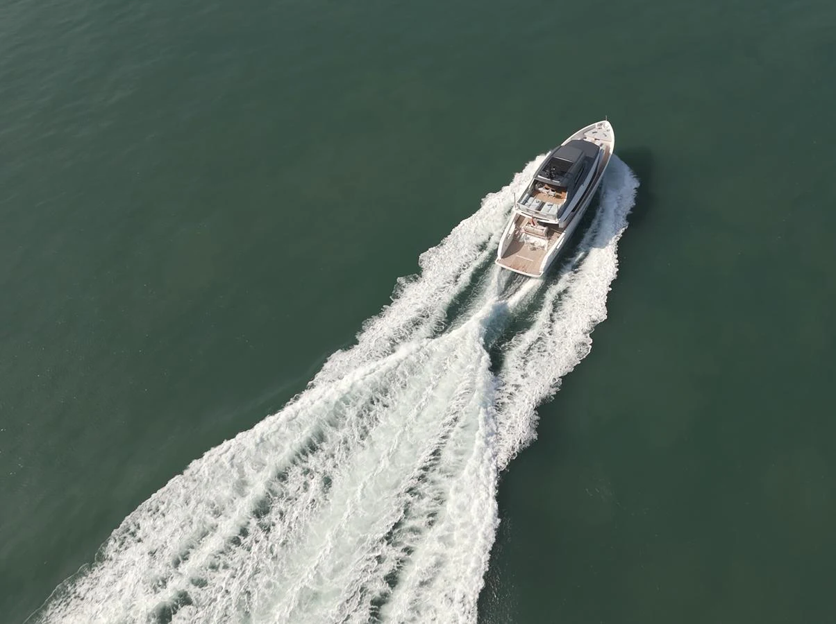 A sleek yacht cruises through calm waters, leaving a trail of white wake behind. aboard SX76 #144 Yacht for Sale