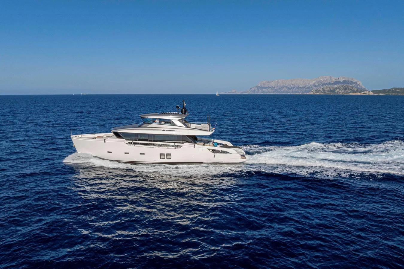 A sleek yacht cruises through deep blue waters with a scenic coastline in the background. aboard FIREFLY Yacht for Sale