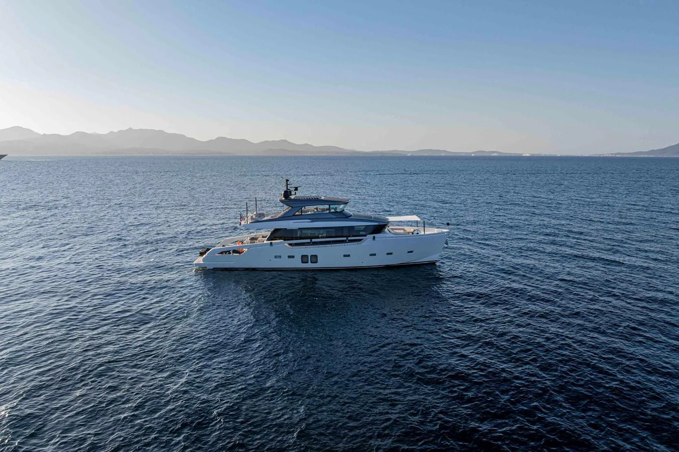 A sleek and modern yacht glides gracefully on calm waters with a stunning backdrop of distant mountains. aboard FIREFLY Yacht for Sale