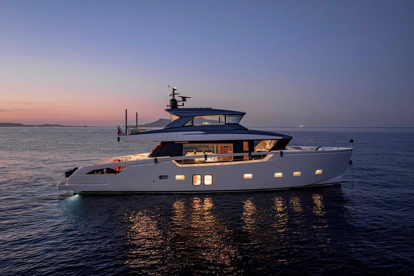 A sleek yacht is illuminated against a serene twilight backdrop on calm waters. aboard FIREFLY Yacht for Sale
