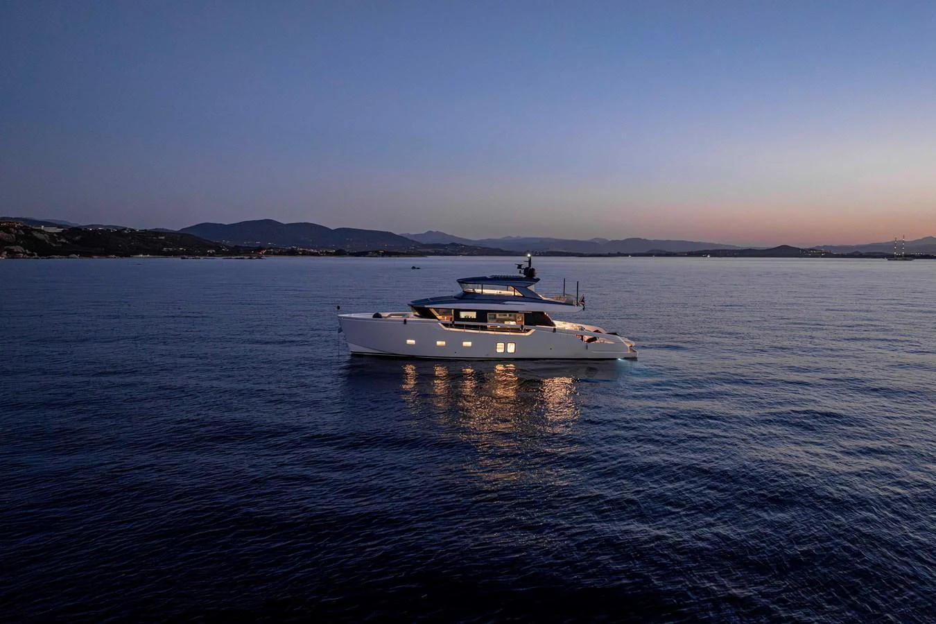 A sleek yacht cruises on calm waters at dusk, illuminated by soft onboard lighting. aboard FIREFLY Yacht for Sale