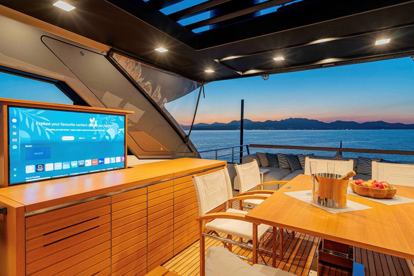 The aft deck offers a luxurious outdoor dining area with a retractable TV and stunning sunset views. aboard FIREFLY Yacht for Sale