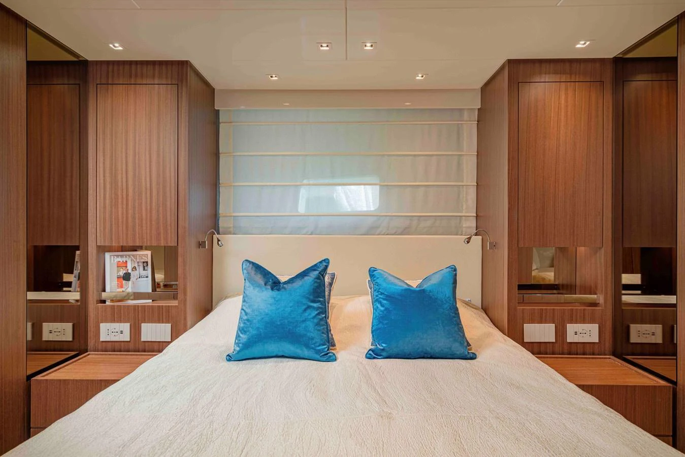 The stateroom features a plush bed with vibrant blue pillows and elegant wooden cabinetry. aboard FIREFLY Yacht for Sale