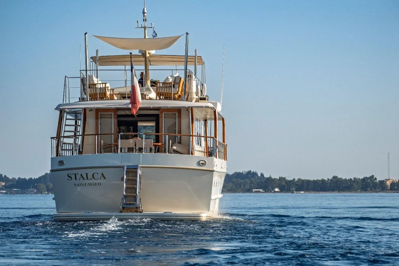 A classic yacht cruises serenely on calm waters, showcasing its elegant aft deck and upper deck lounge area. aboard STALCA Yacht for Sale