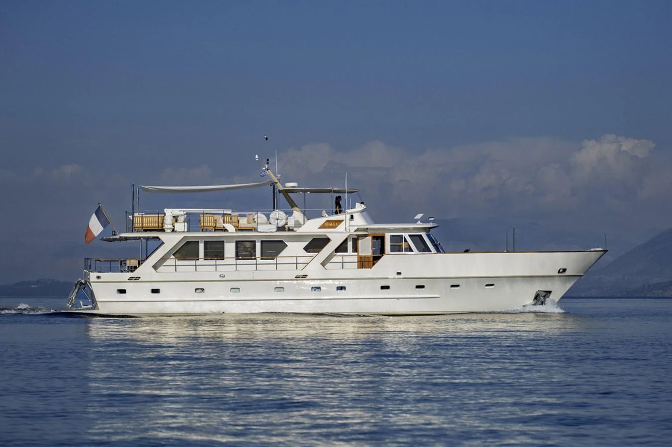 A classic motor yacht cruises gracefully on calm waters under a clear sky. aboard STALCA Yacht for Sale
