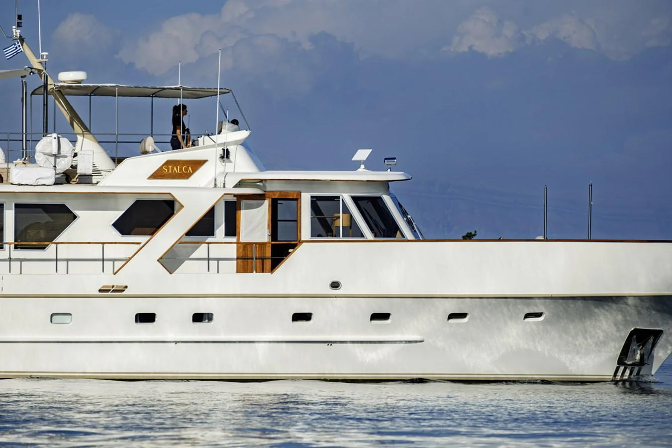 A classic yacht with a sleek white exterior glides gracefully on calm waters under a serene sky. aboard STALCA Yacht for Sale