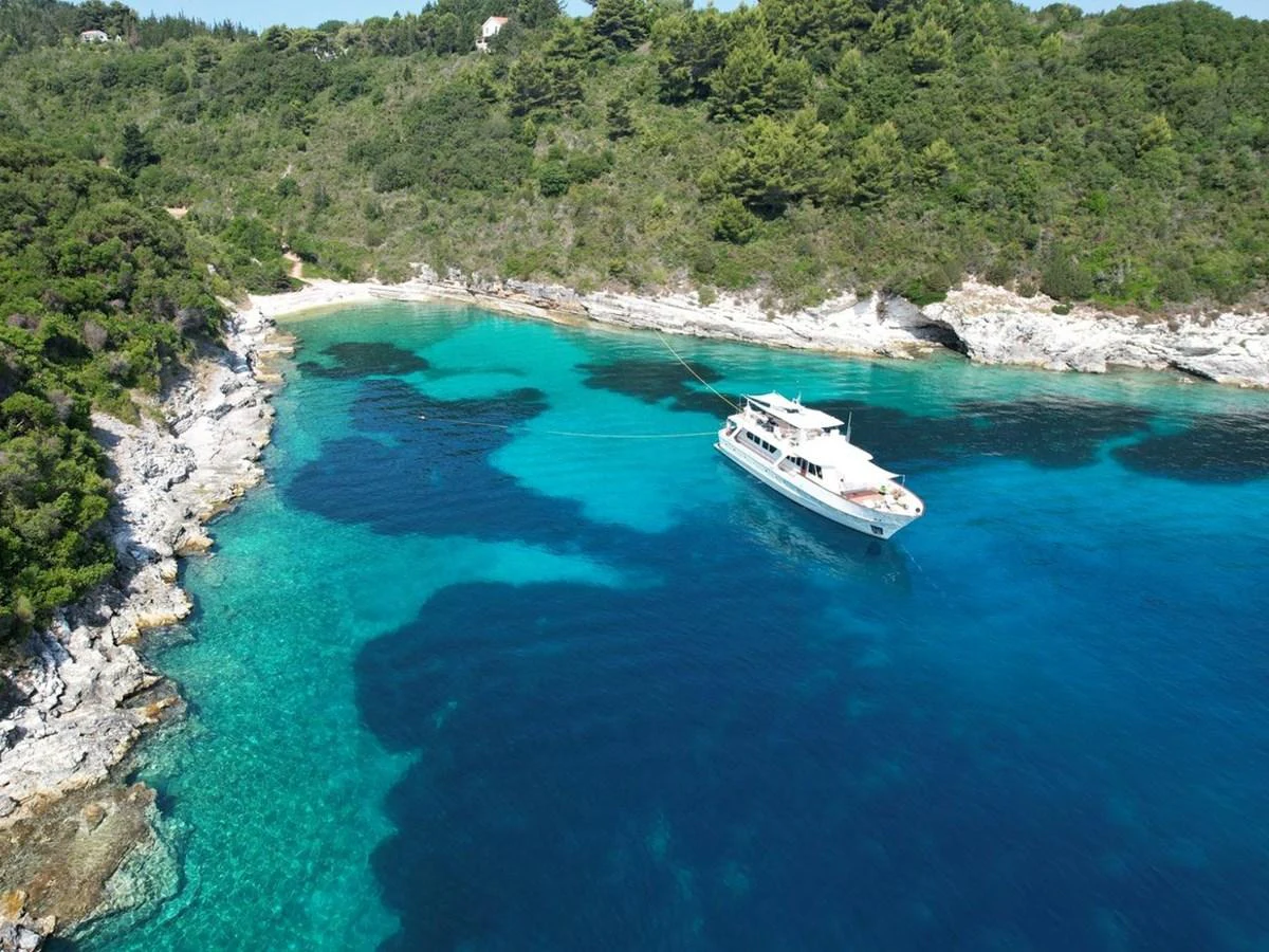 A luxurious yacht is anchored in a serene, turquoise bay surrounded by lush greenery and rocky shores. aboard STALCA Yacht for Sale
