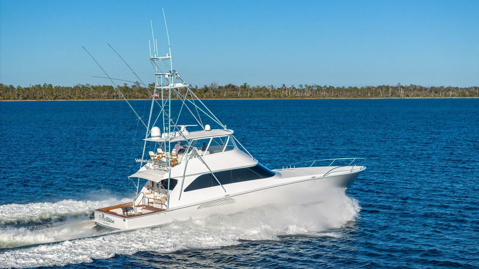 A sleek yacht cruises swiftly on the open water under a clear blue sky. aboard FIRST BITE Yacht for Sale